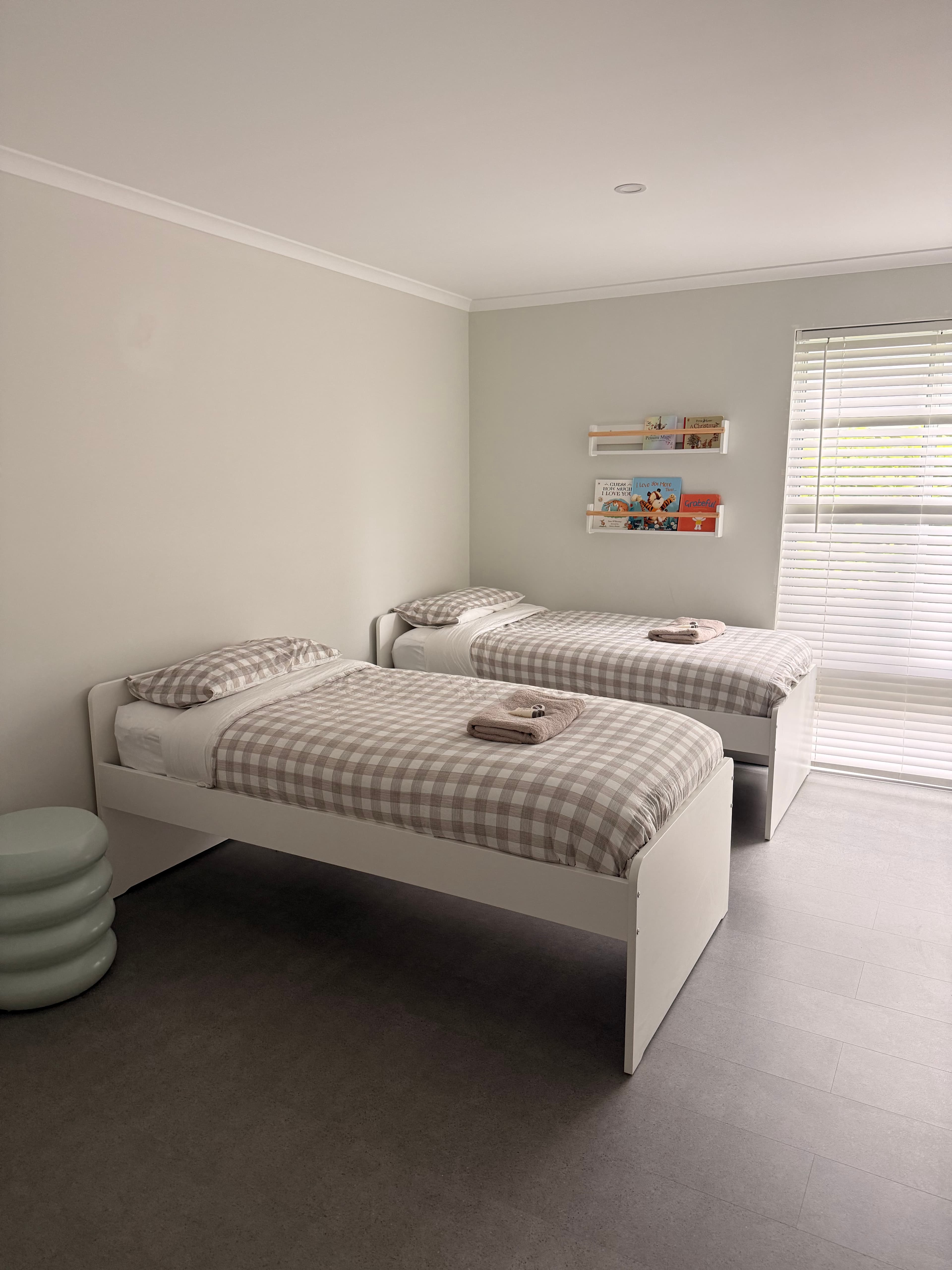 Two white twin beds with beige checkered bedding in a minimalist room with book shelves.