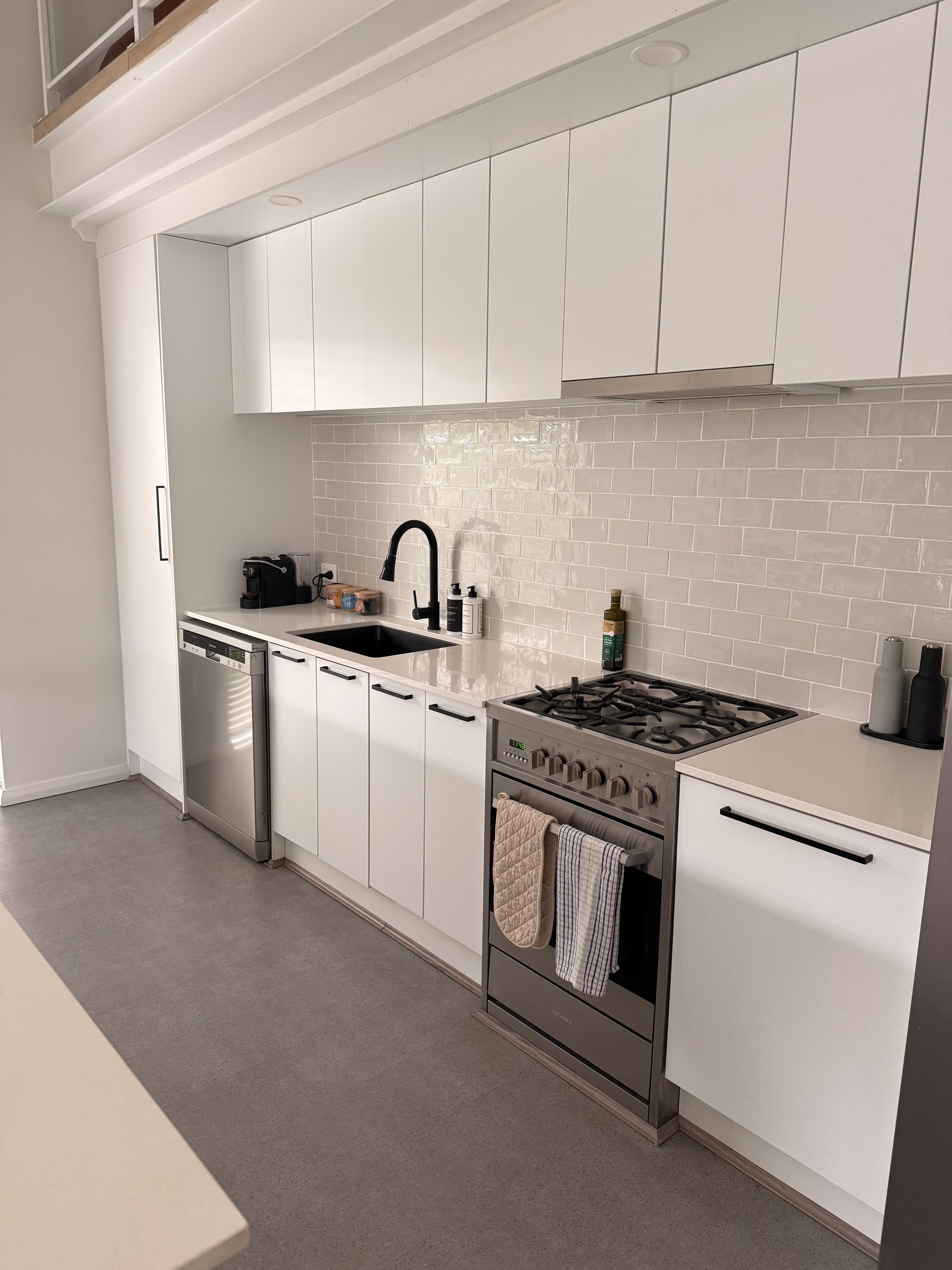 Modern white kitchen with subway tile backsplash, black faucet, and stainless steel appliances.