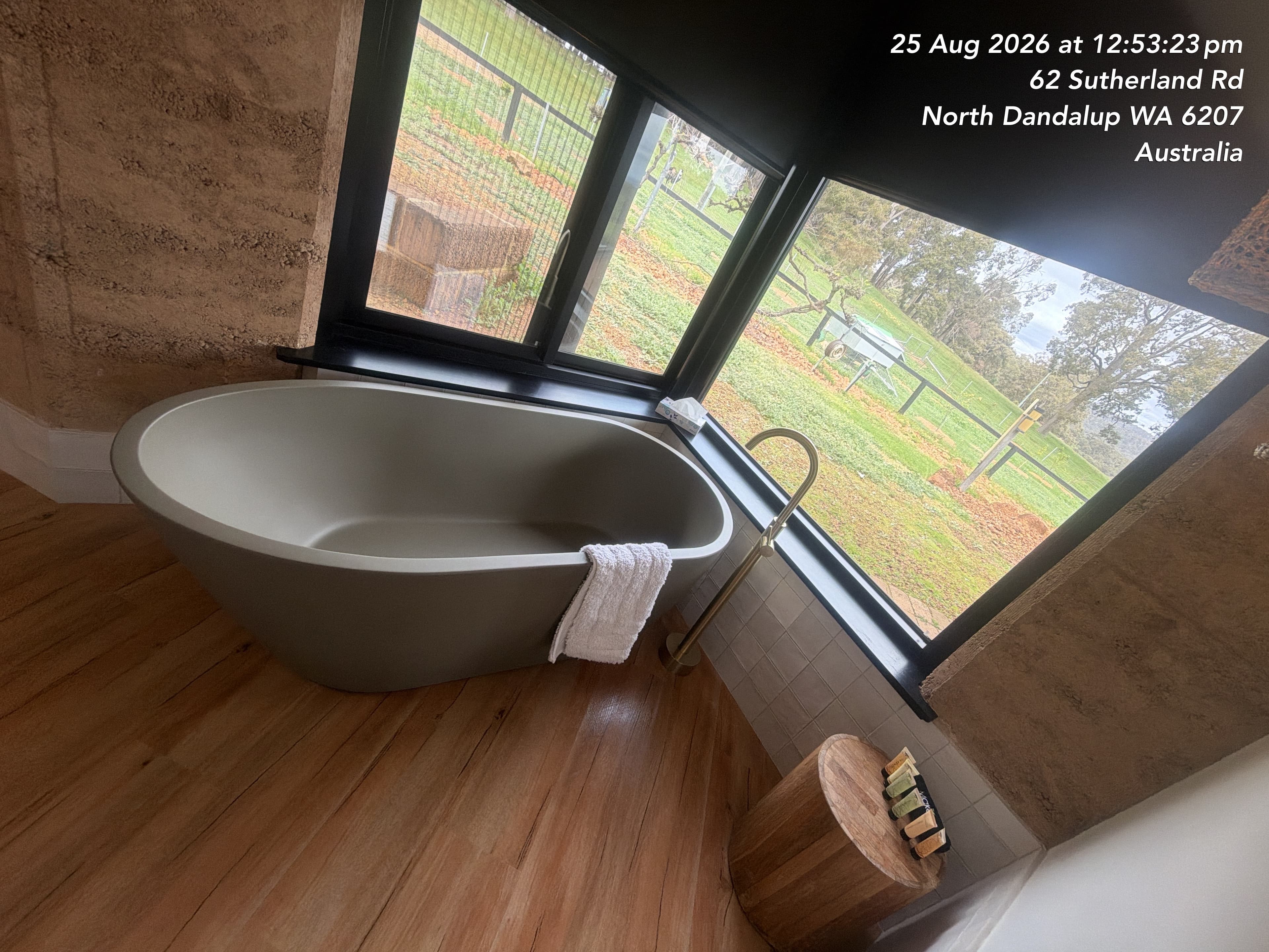 Modern grey freestanding bathtub beside large windows overlooking a lush green rural landscape.