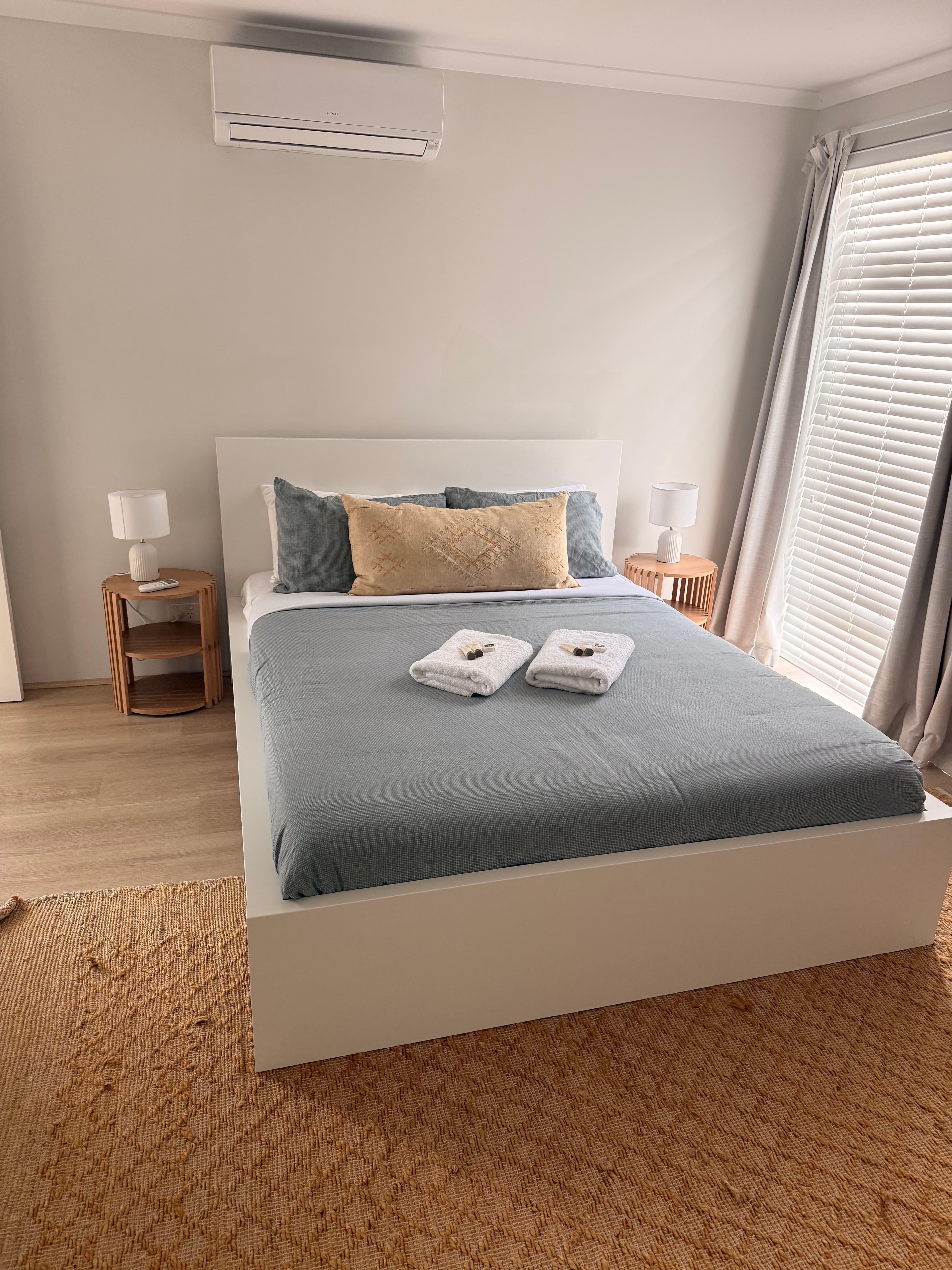 Modern bedroom featuring a white bed with blue linens, wooden nightstands, and a woven rug.