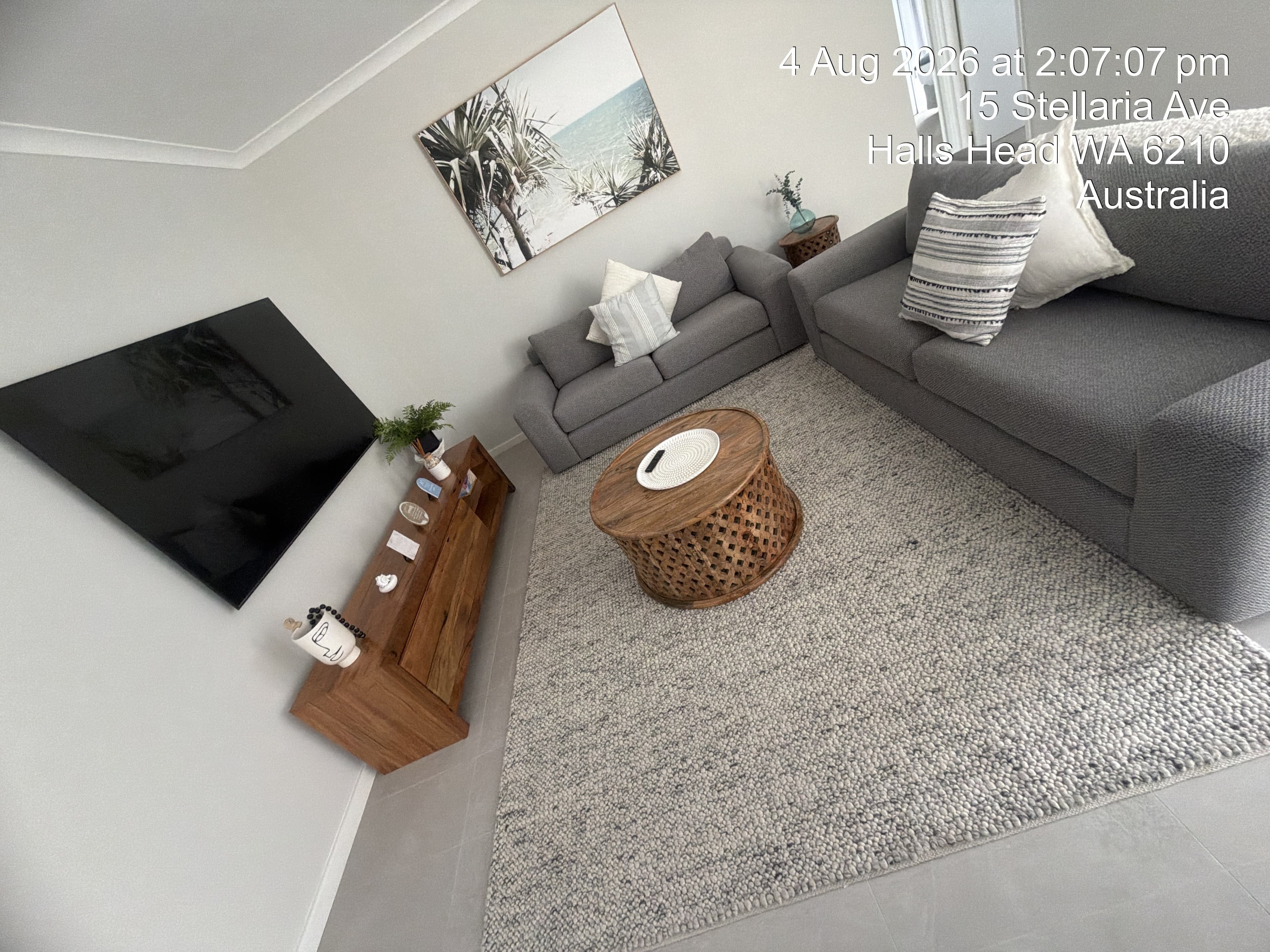 Modern living room with grey sofas, a round wooden coffee table, and a large TV.