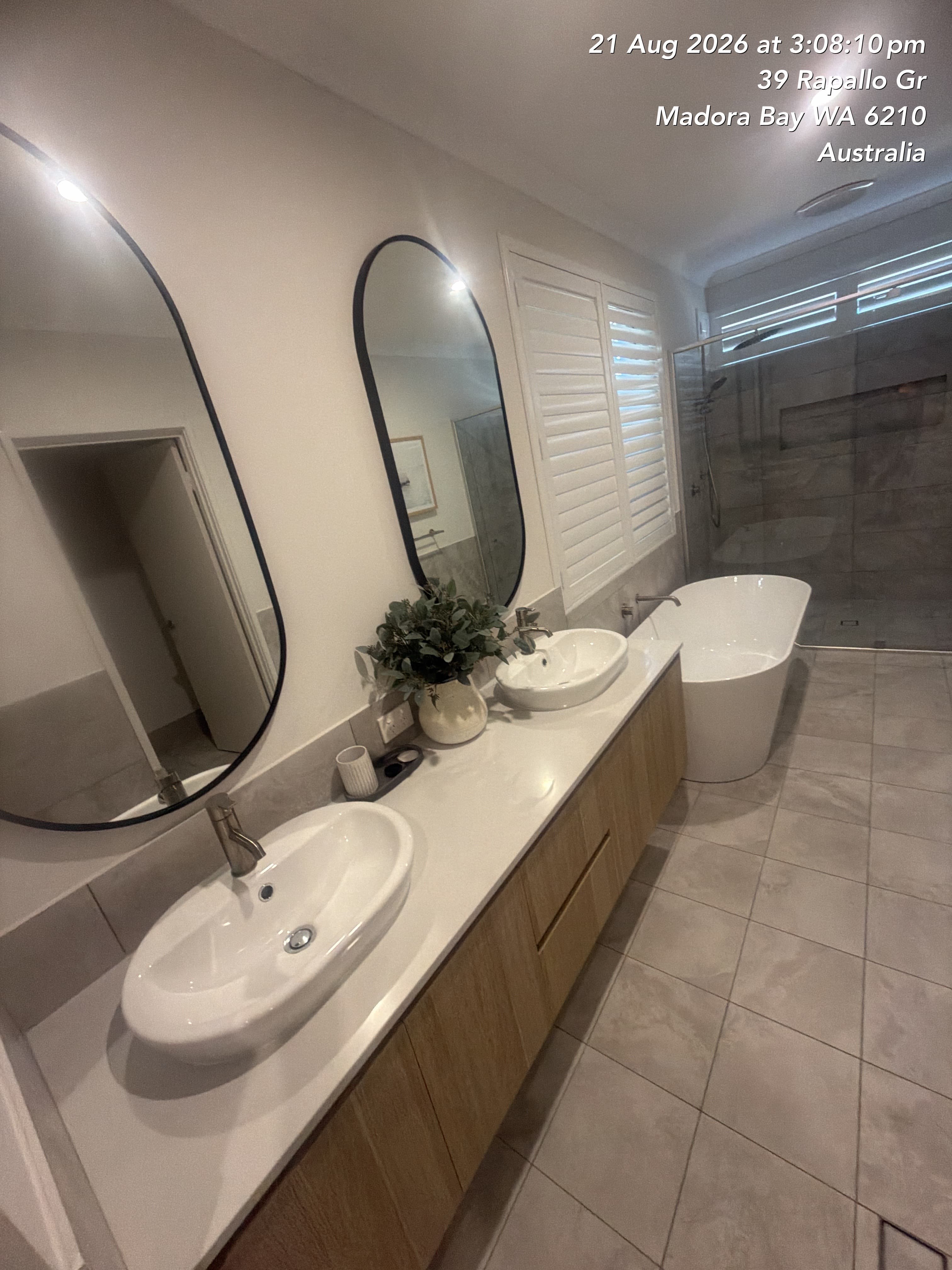 Modern bathroom with double vanity, black-framed oval mirrors, white vessel sinks, and a freestanding bathtub.